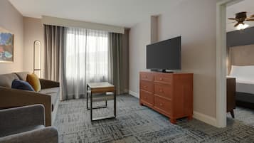 Ein Hotelzimmer mit einer Couch, einem kleinen Tisch, einem Fernseher auf einer Holzkommode und einem Bett mit Kopfteil.