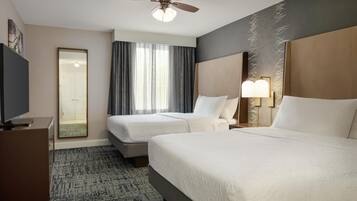 A hotel room with two beds, a ceiling fan, a TV, and a large window with curtains.