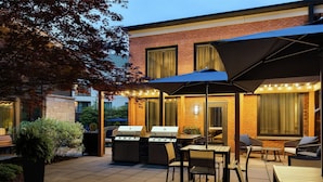 An outdoor patio with a brick building, a grill, and outdoor seating. - Homewood Suites by Hilton Burlington (South Burlington)