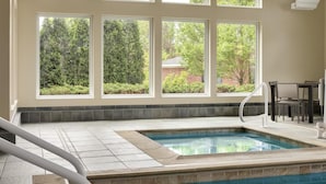 A swimming pool with a view of trees and a brick building through large windows. - Homewood Suites by Hilton Burlington (South Burlington)