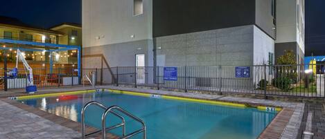 Una piscina interior con superficie de agua cristalina, rodeada por un pavimento de ladrillo y barandillas metálicas.