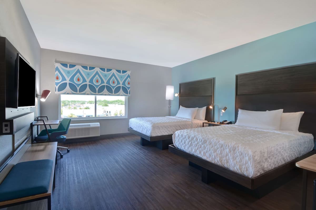 A hotel room with two beds, a desk, a chair, and a TV.