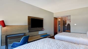 A hotel room with a bed, a desk, a chair, a TV mounted on the wall, and a door leading to another room.