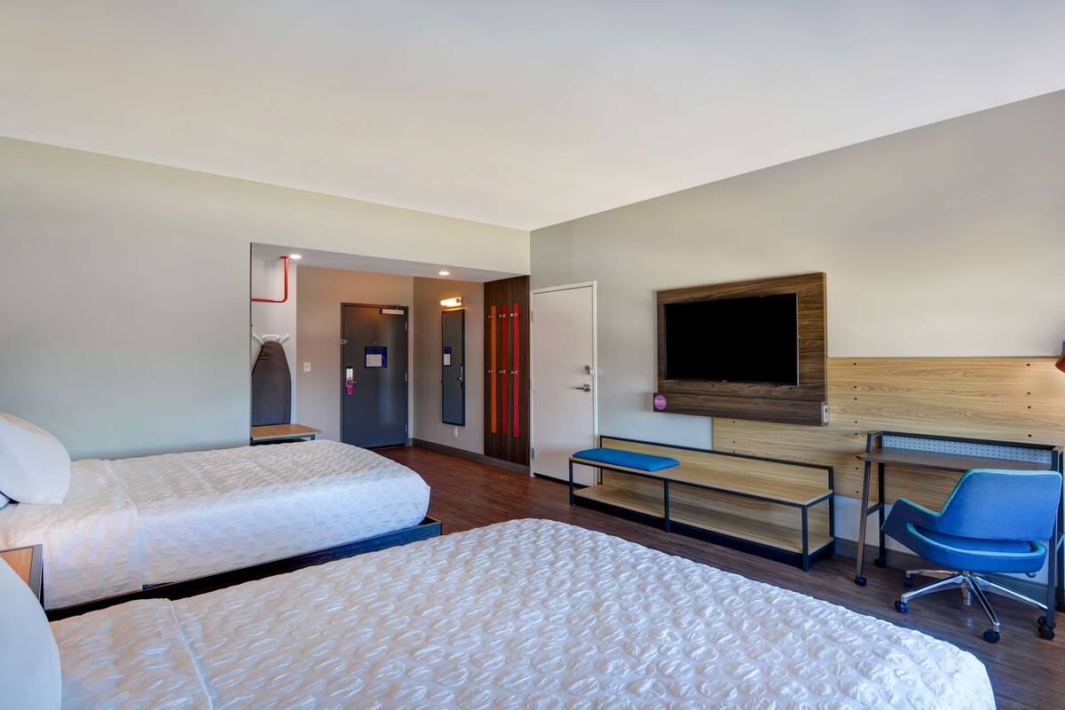A hotel room with two beds, a desk, a chair, a TV, and a wardrobe.