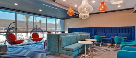 Ein moderner Lounge-Bereich mit einem blauen Sofa, Türkis-Farbenen Sesseln und hängenden, orange-weißen Pendelleuchten.