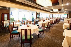 A spacious dining area with round tables and chairs, large windows, and a patterned carpet. - Marroad Inn Tokyo (Fuchu)
