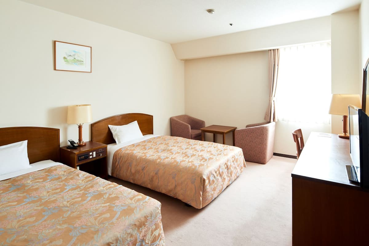 A hotel room with two beds, a desk, a chair, and a small table.