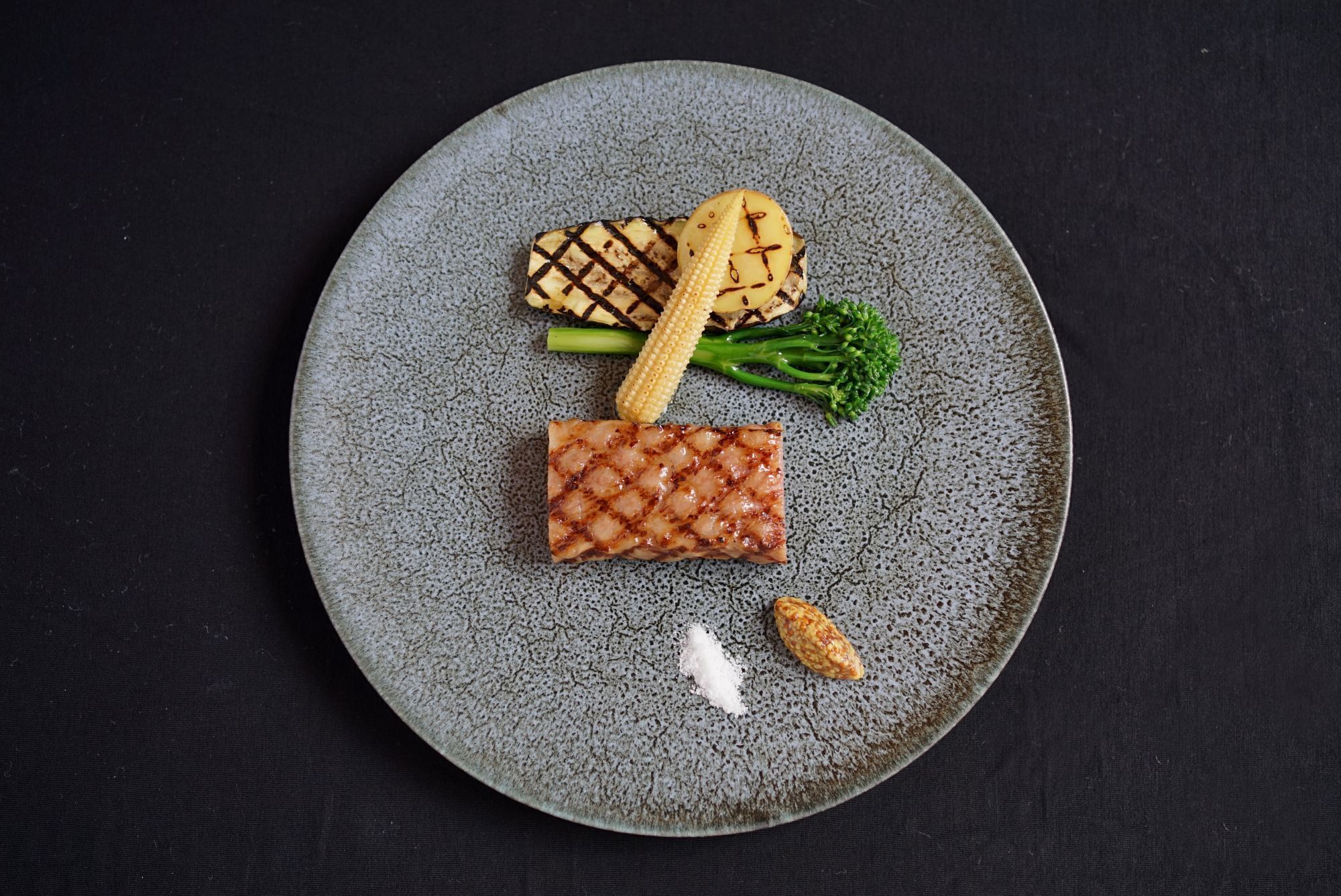 Un plato con carne a la parrilla, maíz, brócoli y un trozo pequeño de queso.