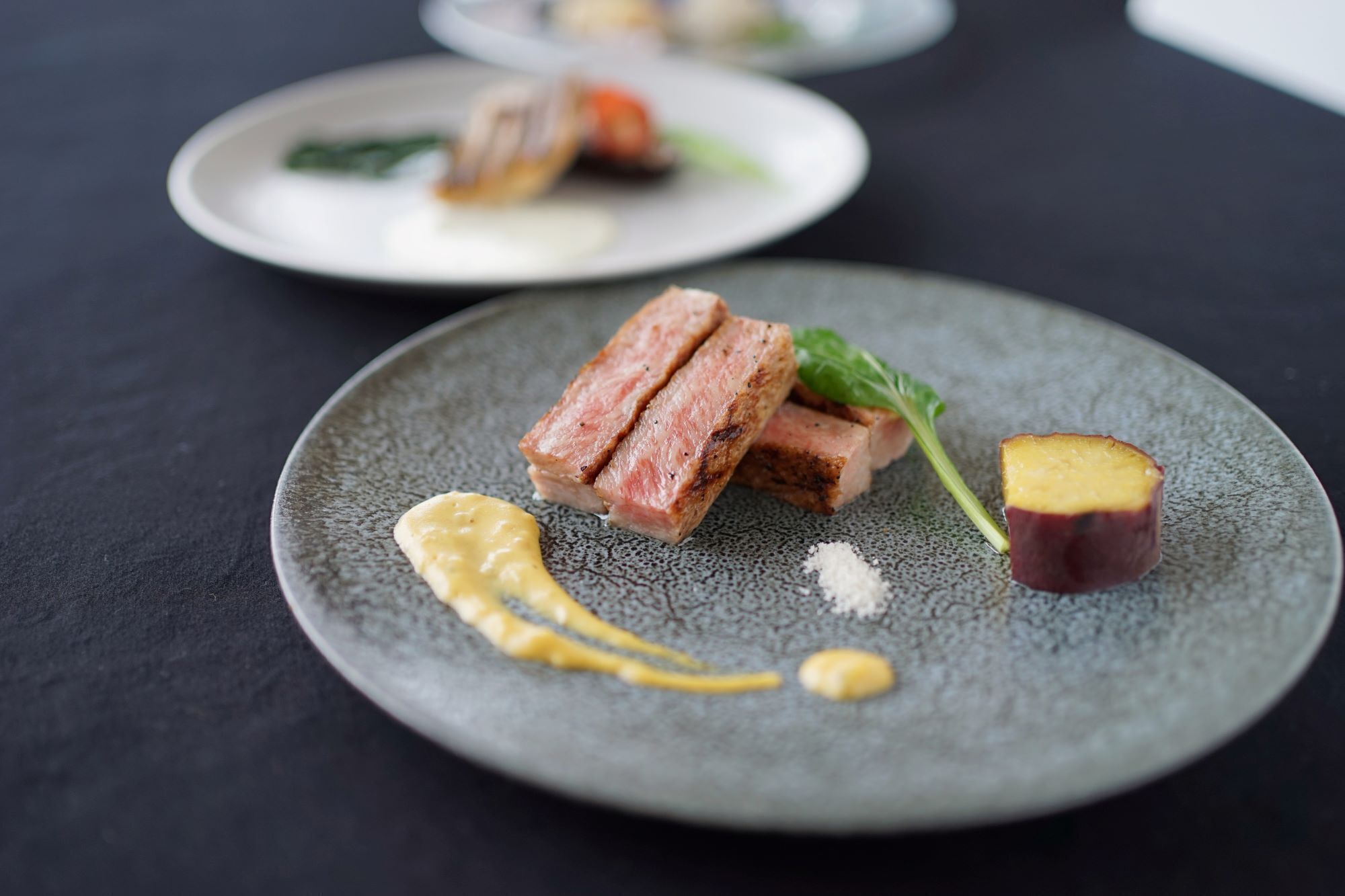 A plate with sliced meat, a piece of fruit, and a sauce.