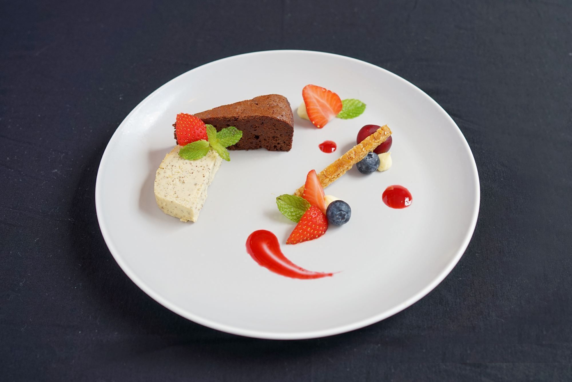 A dessert plate with a brownie, cheesecake, and fruit on a white plate.