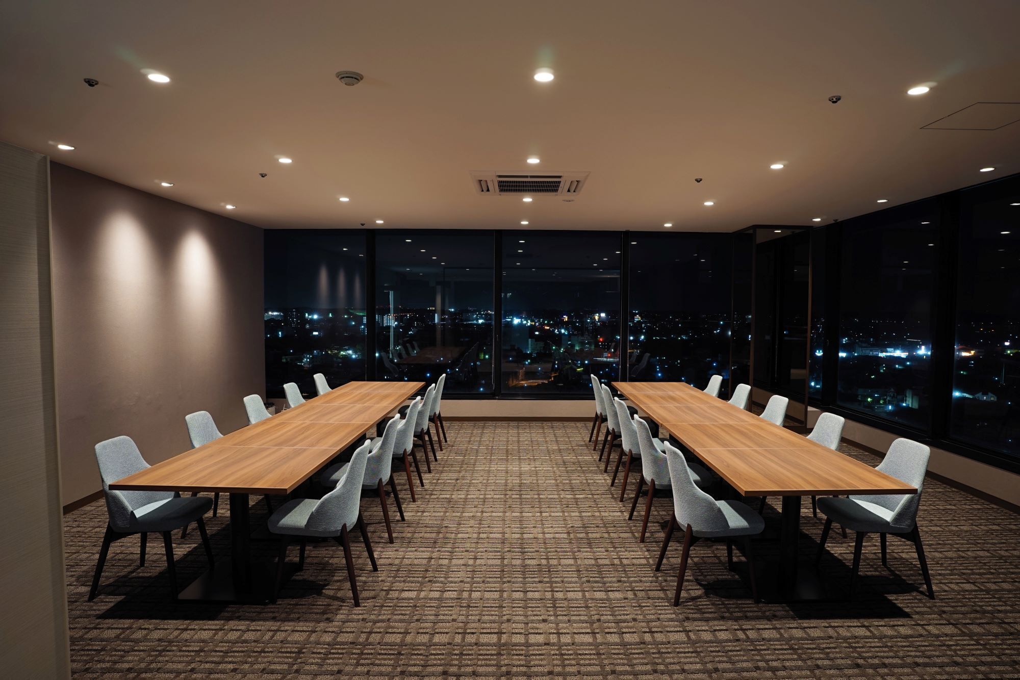 Un salón de conferencias con una larga mesa y sillas, amplias ventanas con vistas a la ciudad e iluminación empotrada en el techo.