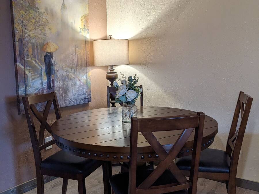 Uma mesa de jantar redonda de madeira com quatro cadeiras, um vaso com flores e um quadro na parede.