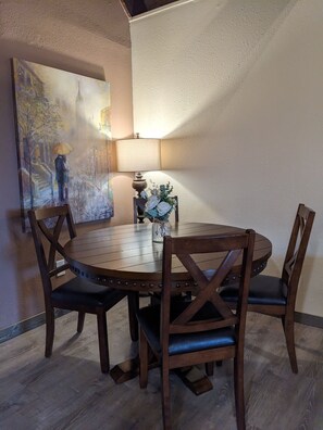A round wooden dining table with four chairs, a vase with flowers, and a painting on the wall. - Wanderlust Inn (Ocean Shores)