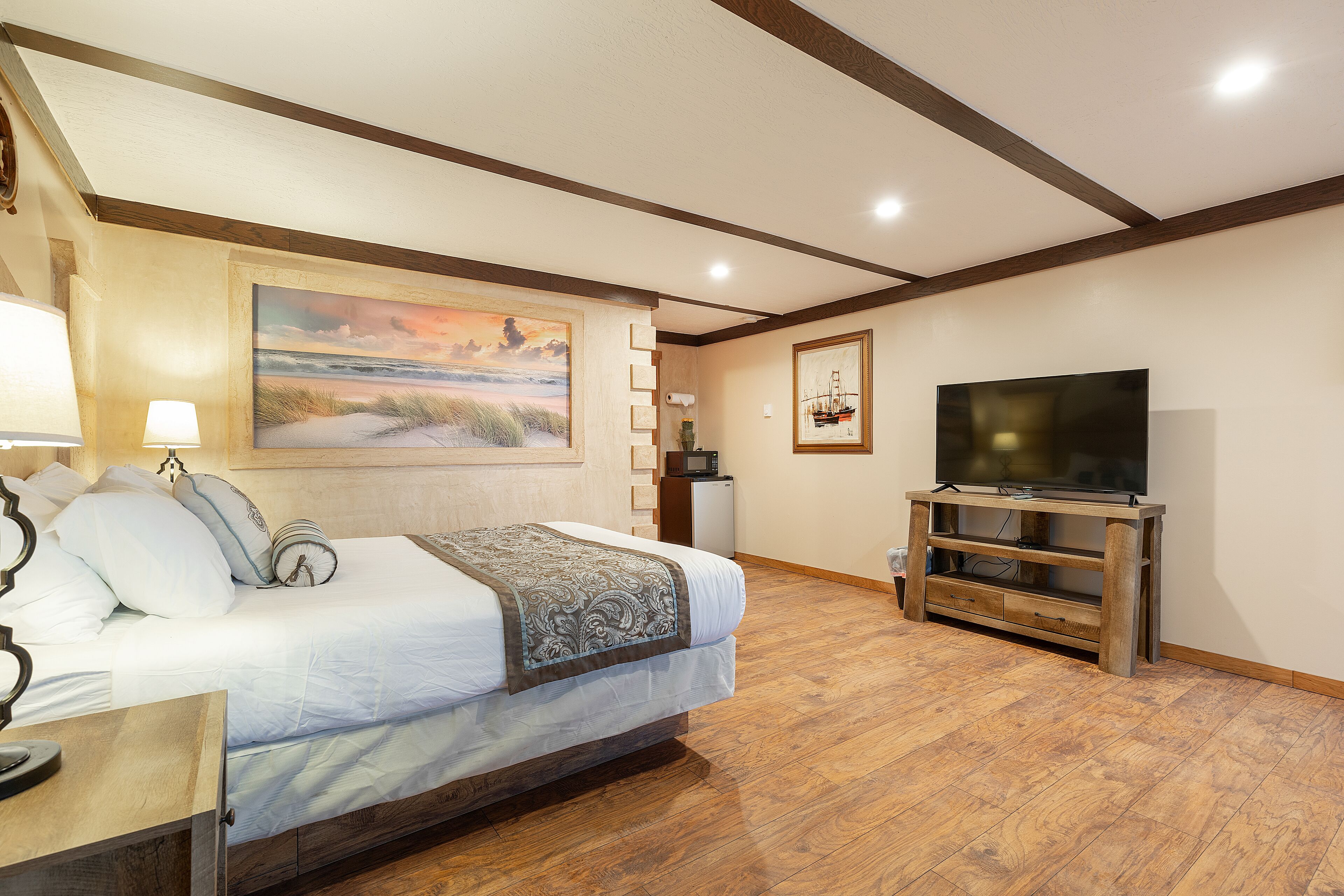Een slaapkamer met een bed, nachtkastje, lamp, schilderij, tv-meubel en houten vloer.
