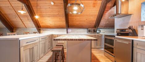 A kitchen with wooden beams, a large island with stools, stainless steel appliances, and pendant lighting.