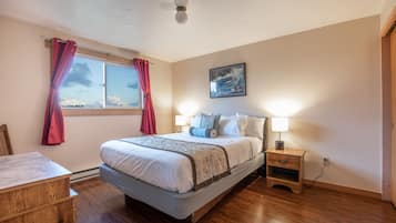 A bedroom with a bed, bedside tables, a window with curtains, a painting on the wall, and wooden flooring.