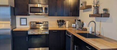 A modern kitchen with dark cabinets, stainless steel appliances, and wooden countertops.