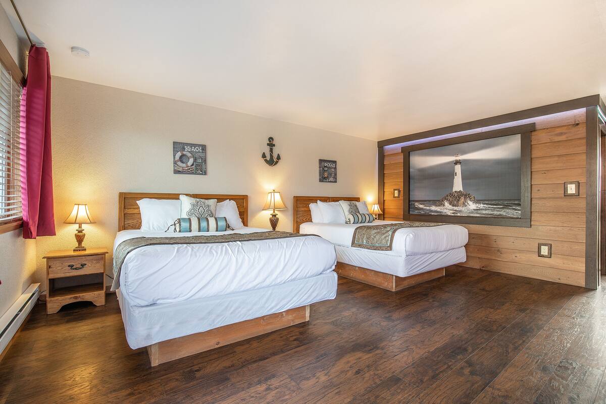 Habitación de hotel con dos camas, suelo de madera y un ventanal con un cuadro de un faro.