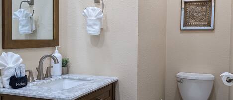 A bathroom with a marble sink, wooden cabinets, a toilet, and a framed artwork on the wall.
