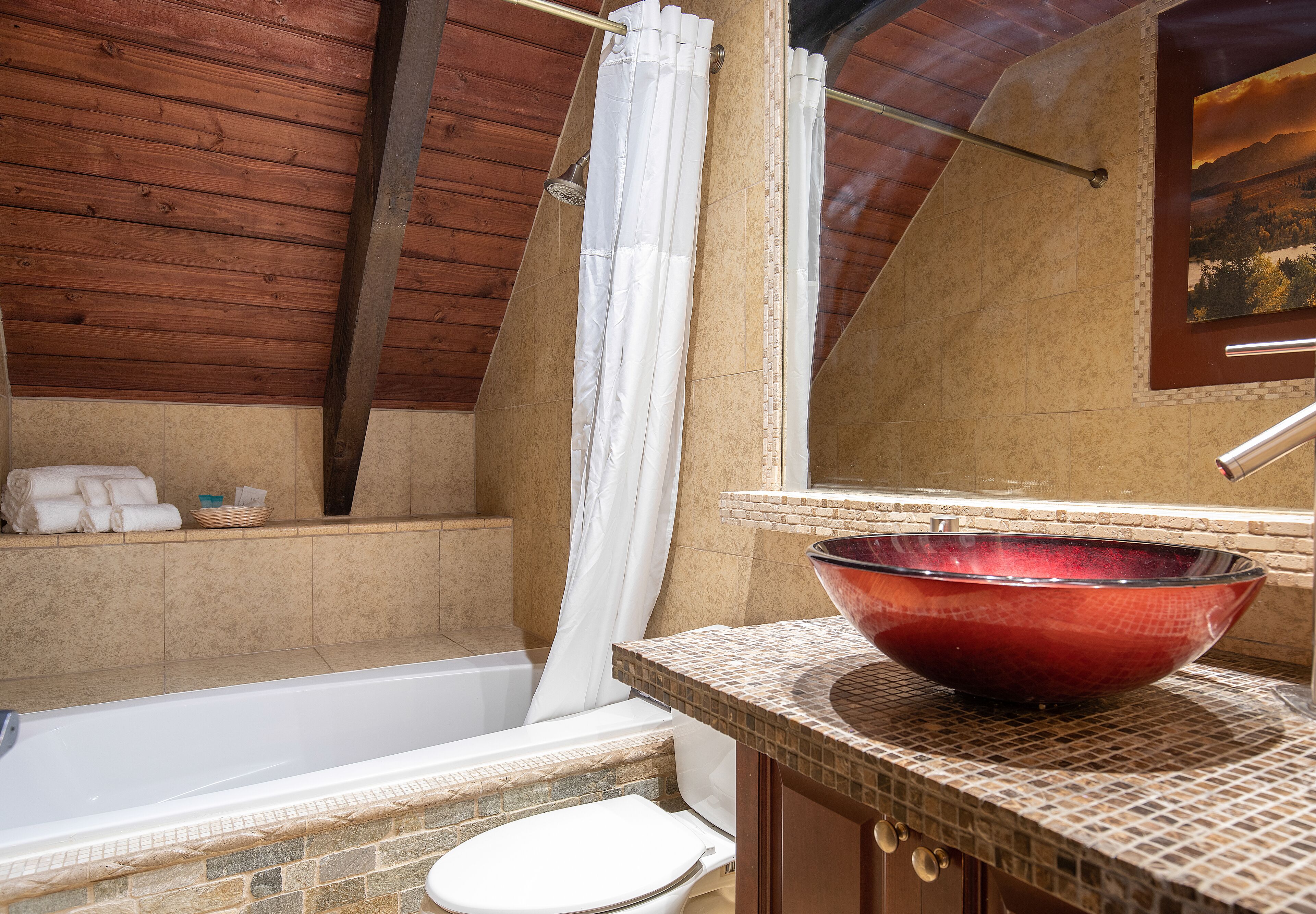 A bathroom with a bathtub, toilet, and a large red bowl sink.