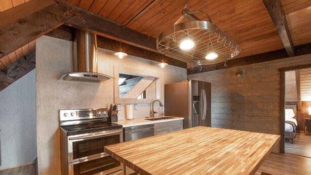 A modern kitchen with stainless steel appliances, a wooden countertop, and a hanging light fixture. - Wanderlust Inn (Ocean Shores)