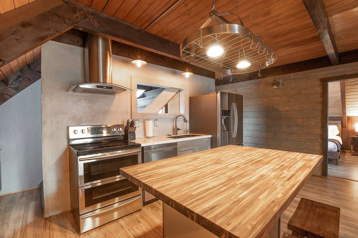 Una cocina moderna con electrodomésticos de acero inoxidable, una encimera de madera y una lámpara colgante.