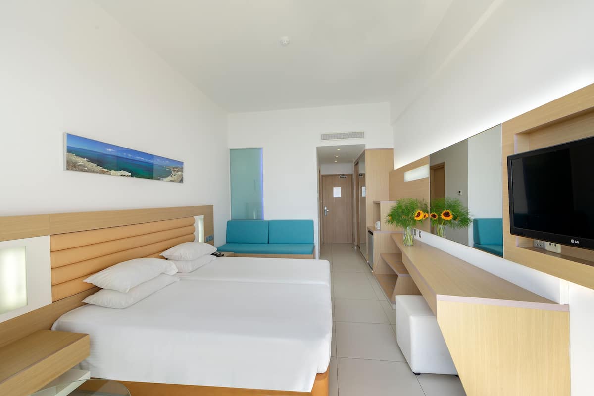 A modern hotel room with a large bed, a seating area, a TV, and a painting on the wall.