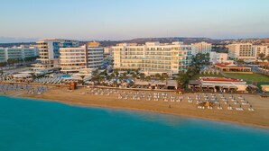 A coastal hotel with multiple buildings, a beach with sun loungers, and a pool area. - Vrissaki Beach Hotel (Paralimni)