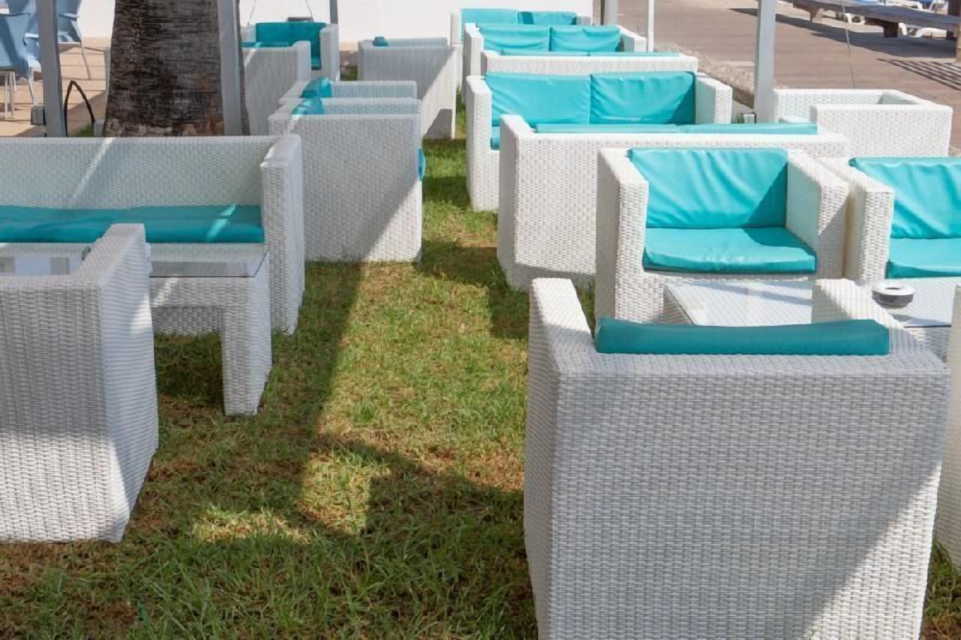 Outdoor wicker furniture with teal cushions arranged on a grassy area.