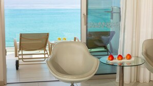 A balcony with a view of the ocean, a wicker chair, a modern armchair, a glass table with fruit, and a sofa. - Vrissaki Beach Hotel (Paralimni)