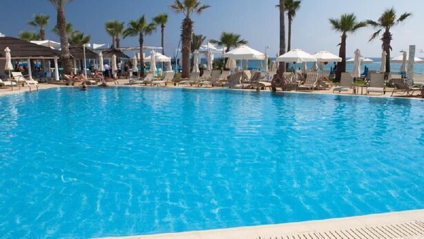 A clear blue pool with lounge chairs and umbrellas, surrounded by palm trees. - Vrissaki Beach Hotel (Paralimni)