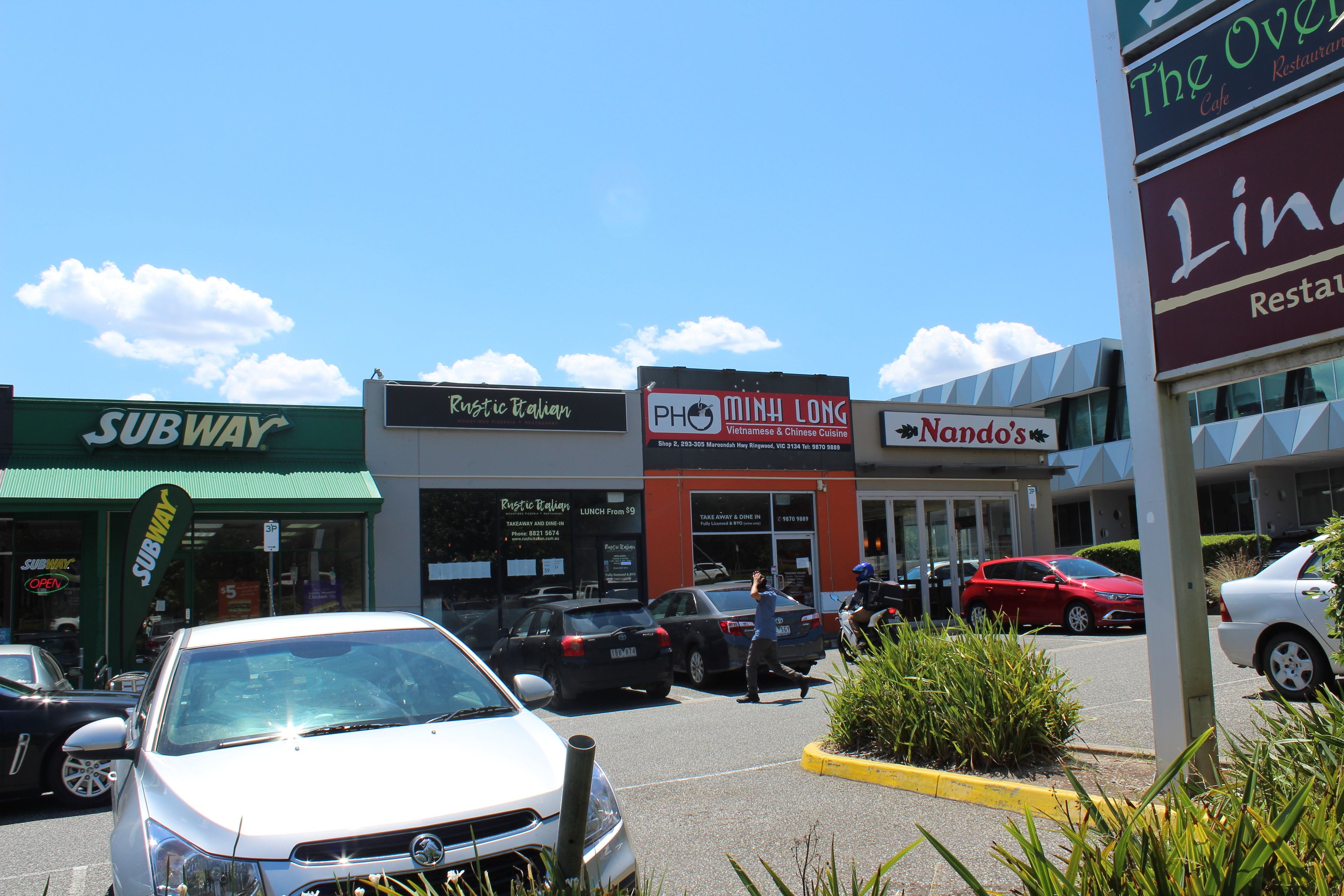 A parking lot with several cars, a Subway restaurant, Rustic Italian, PH MinH Long, and Nando's restaurants.