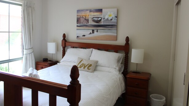 Un lit bien fait, avec des draps blancs et un oreiller sur lequel est brodé le mot « amour ». Au-dessus du lit, on peut voir un tableau représentant une scène de plage.