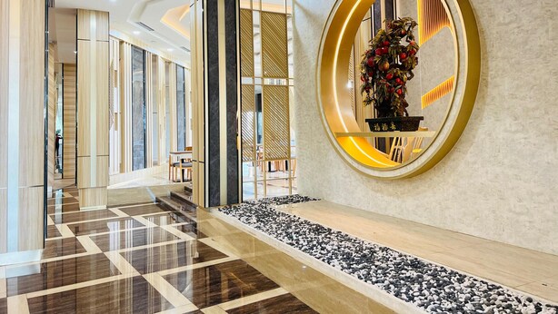 Eine moderne Hotelhalle mit Schachbrettmuster-Boden, einer zentralen Sitzecke und einer Wanddekoration mit Spiegel und Blumenarrangement.