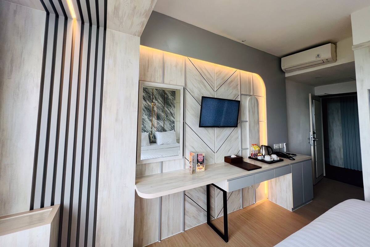 A modern hotel room with a bed, a desk with a flat-screen TV, a minibar, and a window.