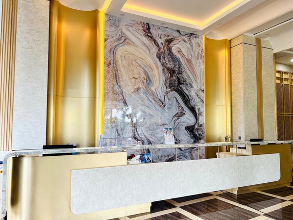 A reception area with a marble wall, a reception desk, and a check-in counter.
