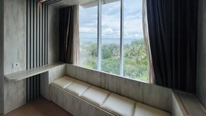 Ein modernes Zimmer mit integriertem Sitzplatz und einem großen Fenster mit Blick auf Stadt und Grünflächen.