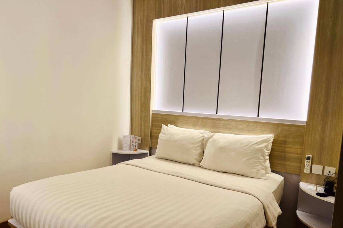 A hotel room with a large bed, a bedside table, a nightstand, and a wall-mounted control panel.