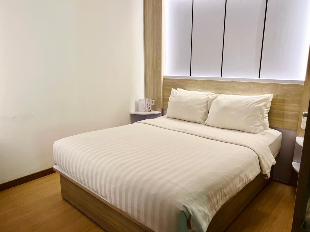 Una cama bien hecha con cabecera de madera y una mesita de noche con lámpara.