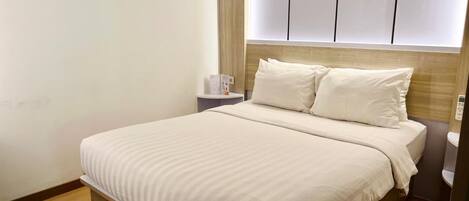 Una cama bien hecha con cabecera de madera y una mesita de noche con lámpara.