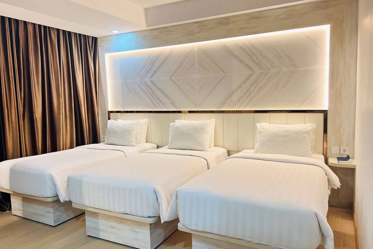 A hotel room with three beds, a marble headboard, and a wooden floor.
