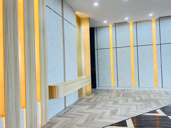 Un moderno vestíbulo de hotel con suelo de patrón espiga, paredes de colores claros con líneas verticales y un banco de madera a lo largo de la pared izquierda.