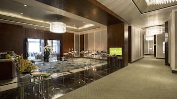 A spacious lobby with a marble floor, modern chandeliers, and a reception area with a digital display.
