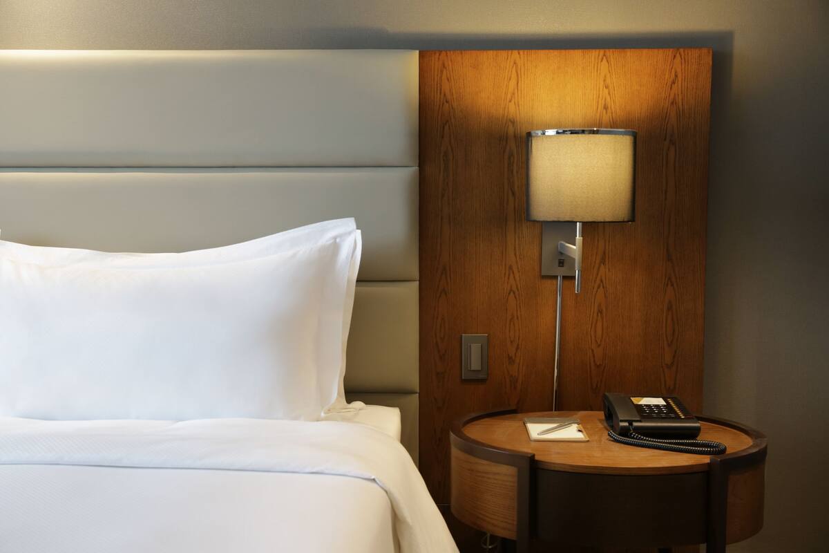 A hotel room with a bed, a bedside table with a lamp, and a telephone.