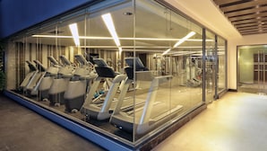 Une salle de sport moderne avec des murs en verre, plusieurs tapis de course et divers appareils d’exercice.