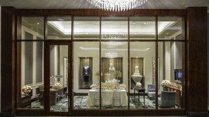 Une salle de banquet avec une grande table dressée pour un événement officiel, entourée de chaises et surmontée d’un lustre.