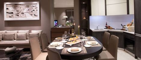 A modern dining area with a round table set for six, a sofa, and a kitchen in the background.