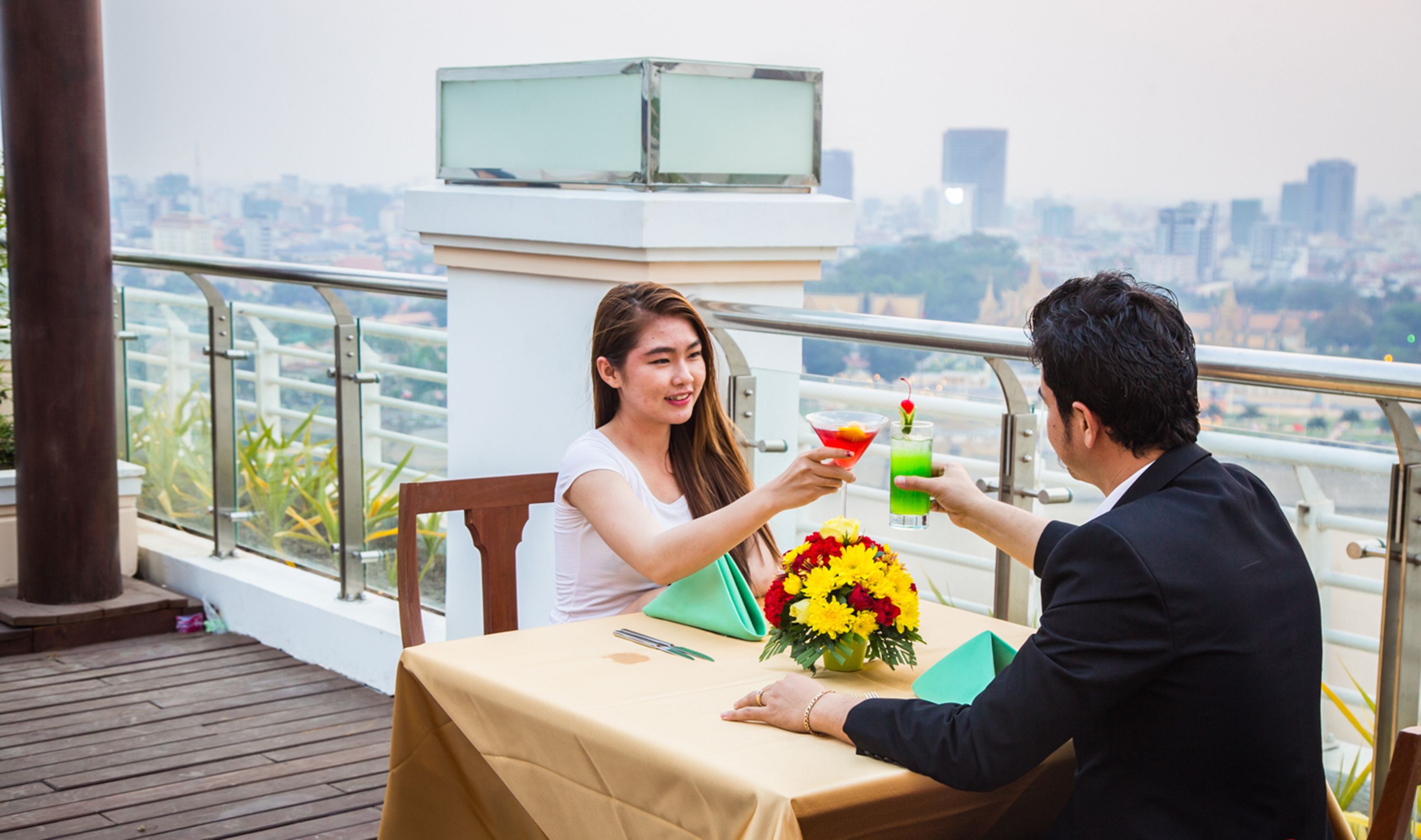 A couple seated at a table with a city view, holding drinks.