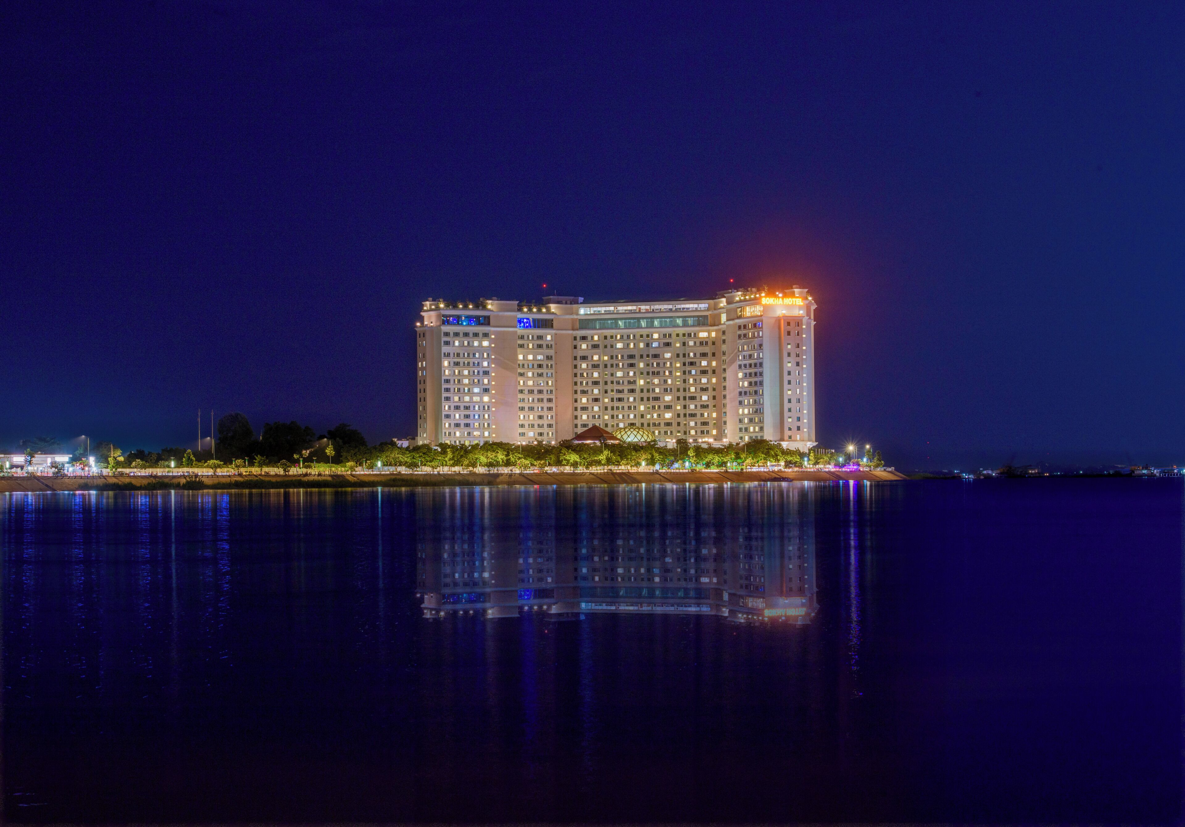 Un hotel moderno de gran altura, con varias plantas, una fachada bien iluminada y su reflejo en el agua.