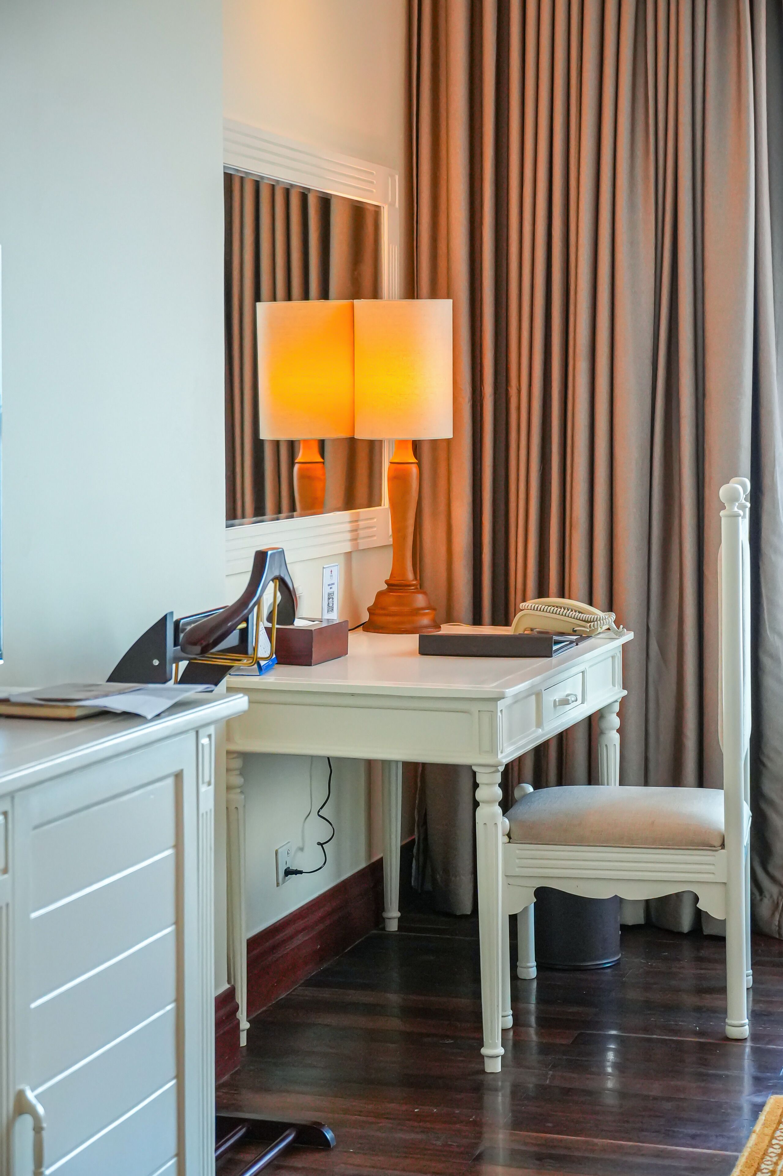 A hotel room with a desk, chair, lamp, and a mirror.